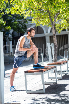 Handsome athlete doing leg stretching on a bench