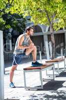 Handsome athlete doing leg stretching on a bench
