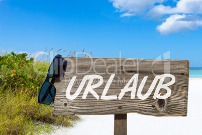 Holzschild mit der Aufschrift "URLAUB" am Sandstrand