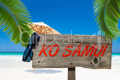 Holzschild mit der Aufschrift "Ko Samui" unter Palmen am Sandstr