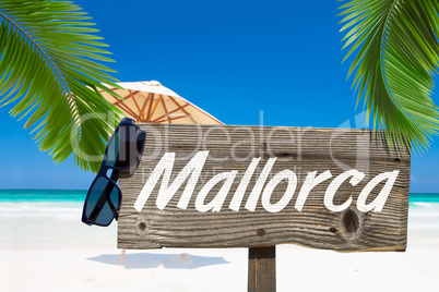 Holzschild mit der Aufschrift "Mallorca" unter Palmen am Sandstr
