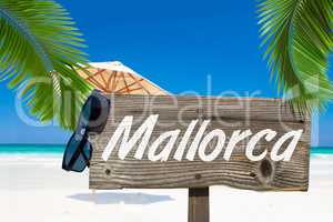 Holzschild mit der Aufschrift "Mallorca" unter Palmen am Sandstr