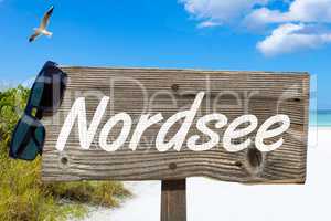 Holzschild mit der Aufschrift "Nordsee" am Sandstrand