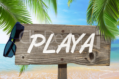Holzschild mit der Aufschrift "PLAYA" unter Palmen am Sandstrand