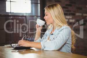 Pretty blonde drinking coffee and writing in planner