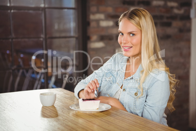 Smiling blonde eating cake and having coffee