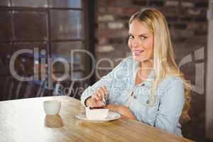 Smiling blonde eating cake and having coffee