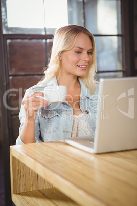 Smiling blonde having coffee and using laptop