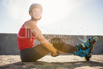 Smiling sporty blonde skater sitting on ground