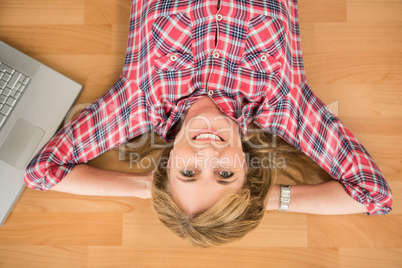 Smiling woman lying on floor next to laptop