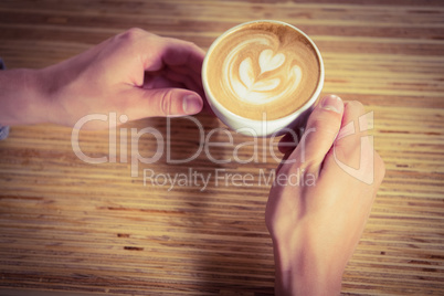 Hands holding cappuccino with coffee art