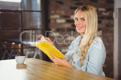Smiling blonde turning the page of yellow book