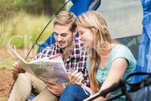 Young pretty hiker couple sitting in a tent looking at map