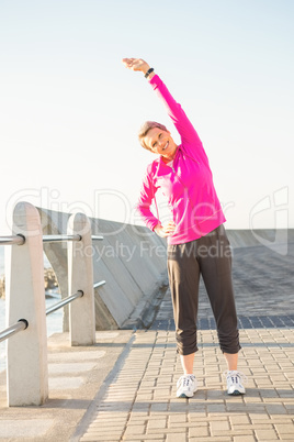Smiling sporty woman stretching at promenade