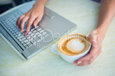 Woman enjoying a cappuccino using laptop