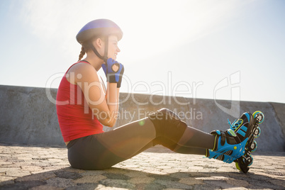 Sporty blonde skater sitting on ground and fastening helmet