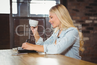 Smiling blonde drinking coffee and writing in planner