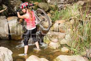 Blonde athlete carrying her mountain bike over stream