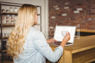 Rear view of blonde having coffee and using laptop