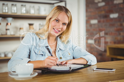 Smiling blonde having coffee and writing in planner