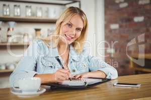 Smiling blonde having coffee and writing in planner