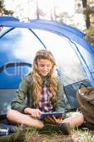 Pretty blonde camper using tablet and sitting in tent