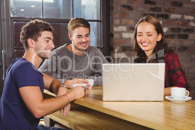 Smiling friends having coffee together and looking at laptop