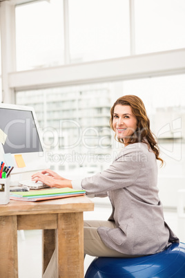 Casual businesswoman sitting on exercise ball while working