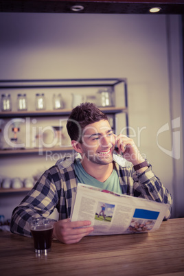 Smiling hipster phoning and holding newspaper