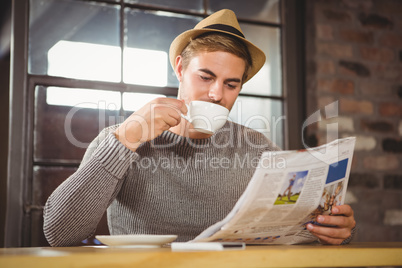 Handsome hipster drinking coffee and reading newspaper