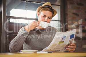 Handsome hipster drinking coffee and reading newspaper
