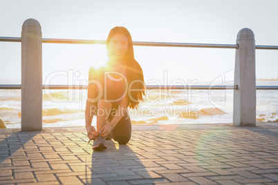 Smiling fit woman tying her shoelace at promenade