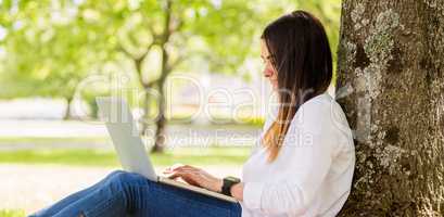 Beautiful brunette using laptop in the park