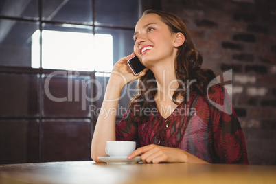 Smiling brunette having coffee and phoning