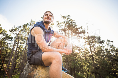 Young happy jogger sitting on rock and looking away