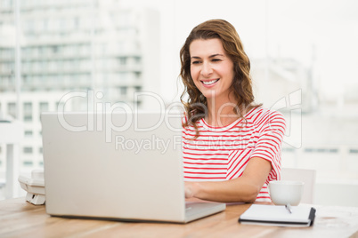 Smiling casual businesswoman using laptop