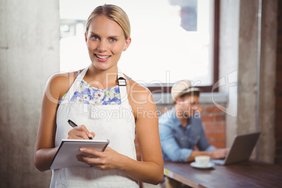 Smiling blonde waitress taking order in front of customer