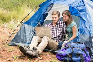 Young pretty hiker couple sitting in a tent looking at laptop