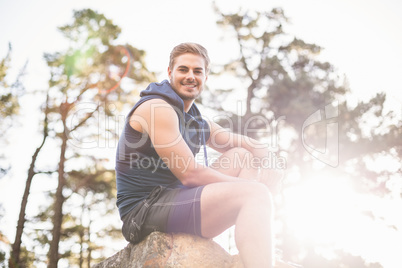 Young happy jogger sitting on rock and looking at camera