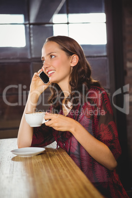 Smiling brunette drinking coffee and phoning