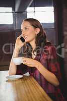 Smiling brunette drinking coffee and phoning