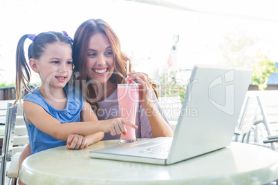 Mother and daughter using laptop at cafe terrace