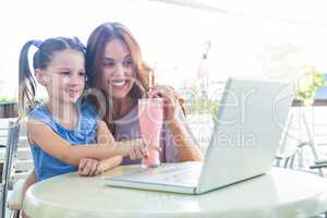 Mother and daughter using laptop at cafe terrace