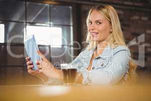 Smiling blonde having coffee and using tablet computer