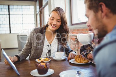 Smiling friends enjoying coffee and looking at tablet