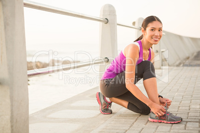 Smiling fit woman tying shoelace at promenade