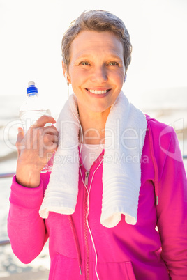 Smiling sporty woman with water bottle listening to music