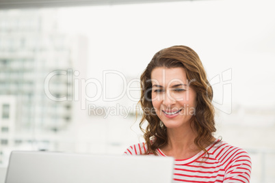 Smiling casual businesswoman using laptop