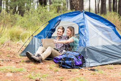 Young pretty hiker couple sitting in a tent looking at laptop