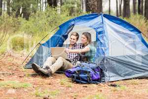 Young pretty hiker couple sitting in a tent looking at laptop